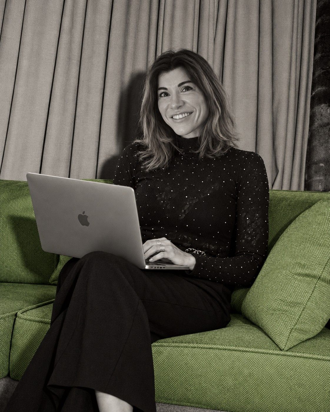 Pia Pucciarello, founder of PP Studio Bespoke, smiling on a green sofa with her laptop