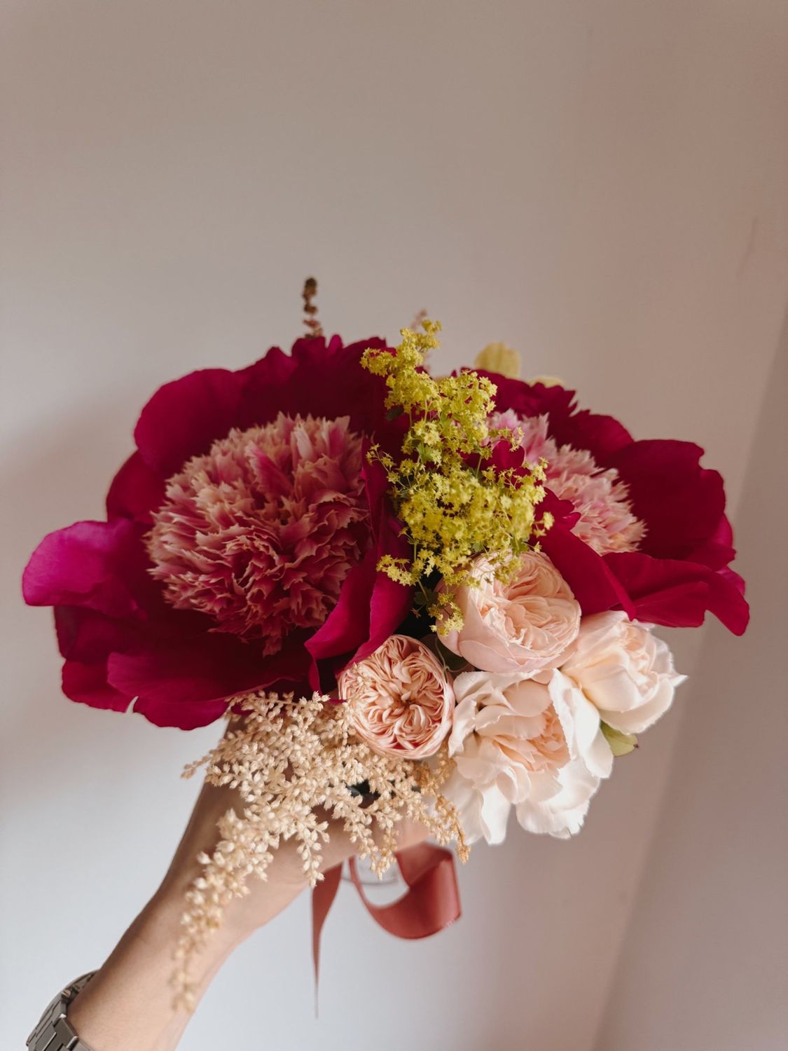 An event arrangement curated by PP Studio: peonies, garden roses, lady's mantle and astilbe tied with ribbon