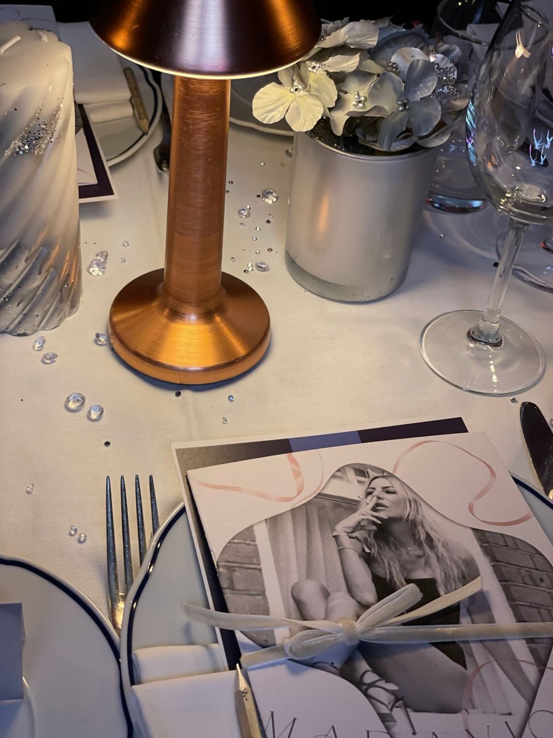Bachelorette dinner at Bagatelle London directed by PP Studio: a silver table with a copper lamp, scattered crystals, silver flowers and the custom brochure tied with velvet ribbon at each place