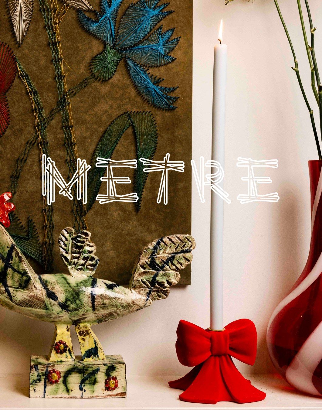 Metre content imagery by PP Studio: a white taper candle in a red velvet bow candlestick beside a glazed ceramic bird and a string-art panel, with the Metre wordmark