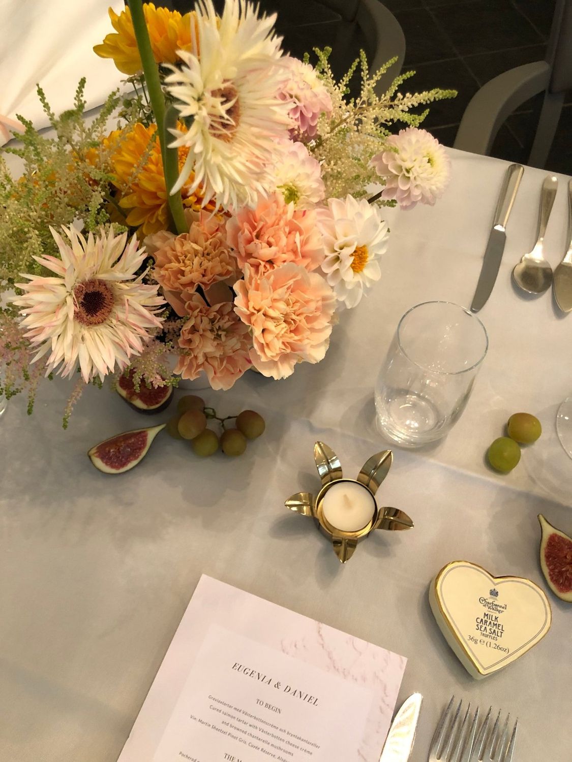 Wedding lunch in Stockholm directed by PP Studio: a table set with peach carnations, dahlias and astilbe, halved figs and grapes, a brass tealight and the printed menu for Eugenia and Daniel
